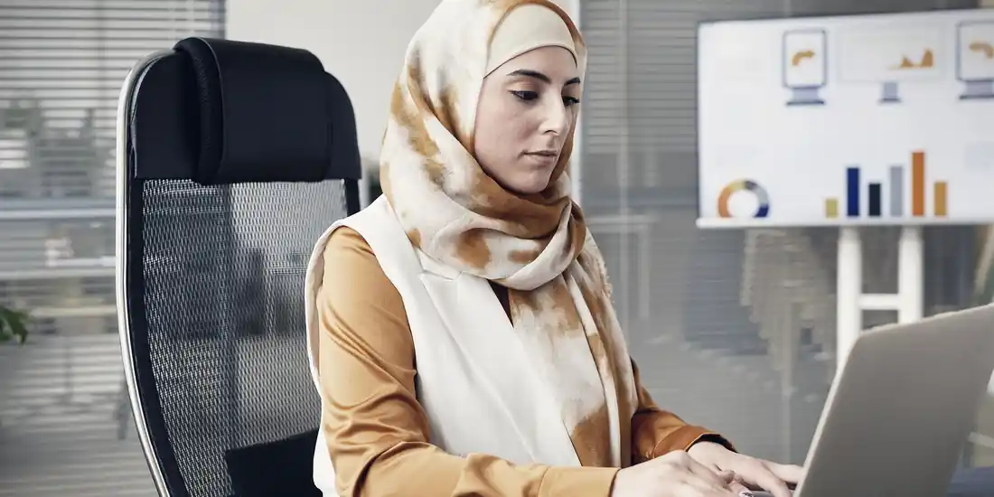 محللة بيانات تعمل على حاسوب محمول أمام لوحة مؤشرات